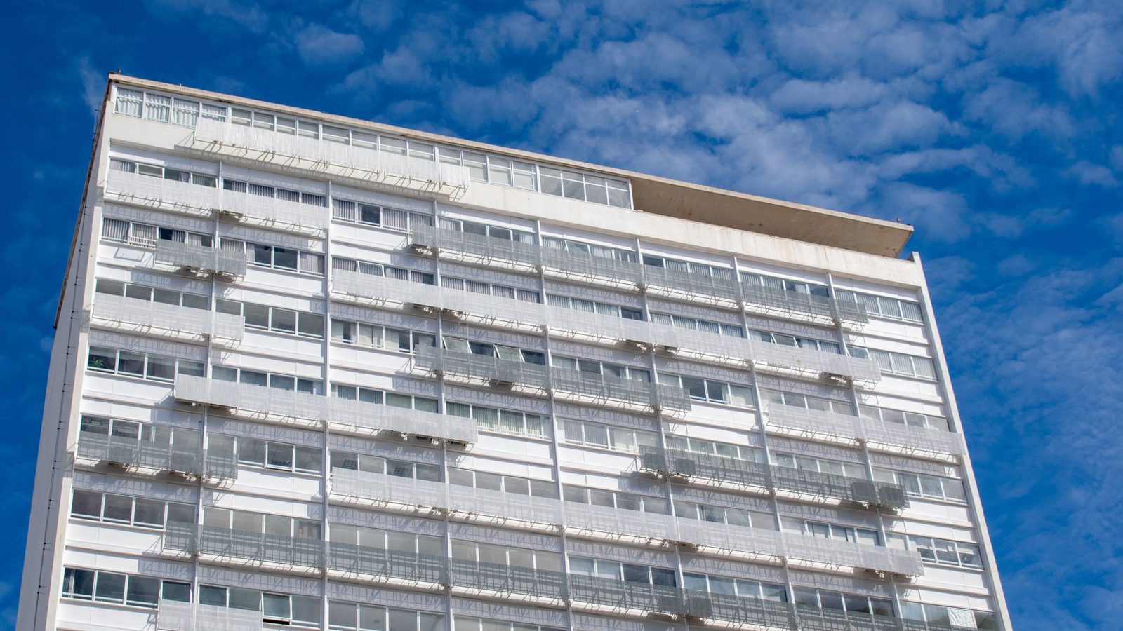 Fachada de bloco residencial em Brasília sob céu azul, com a grelha de janelas típica das superquadras.